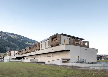 Modernes Mehrfamilienhaus mit Balkonen, Photovoltaikanlage und Bergblick in ländlicher Umgebung.