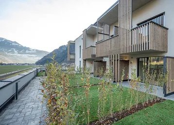 Moderne Wohnanlage mit Holzlamellenbalkonen und Blick auf die umliegende Berglandschaft.