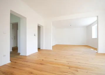 Helles, leeres Wohnzimmer mit neuem Holzboden und offenen Durchgängen zu weiteren Räumen.