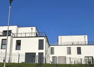 Moderne weiße Gebäude mit Flachdächern und Balkonen unter klarem blauem Himmel.