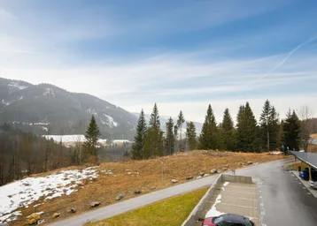 Weitläufiger Blick auf die bergige Landschaft mit Wald und teilweise verschneiten Hängen.