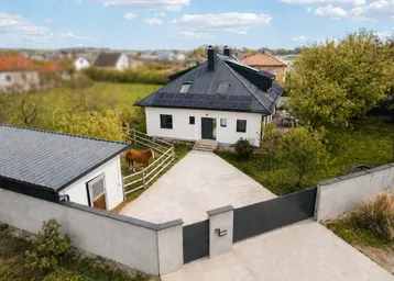 Luftaufnahme eines modernen Einfamilienhauses mit Solaranlage, großem Grundstück und Pferd auf der Weide.