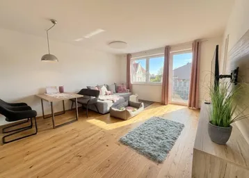 Gemütliches Wohnzimmer mit hellem Parkettboden, Sofa und einem kleinen Esstischbereich.