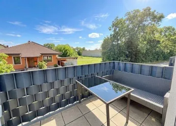 Heller Balkon mit Sitzgelegenheiten und Blick auf die grüne Umgebung und ein Einfamilienhaus.