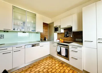 Moderne Küche mit weißen Schränken, integrierten Geräten und braunen Fliesenboden.