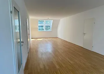 Helles, leeres Wohnzimmer mit Holzparkettboden und Dachschrägenfenstern, bereit zur Einrichtung.