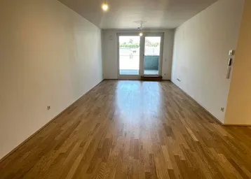 Heller, leerer Raum mit Holzboden und Zugang zu einem Außenbereich durch eine Glastür.
