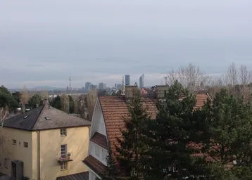 Panoramablick über die Dächer der Stadt mit grünen Bäumen und einer fernen Skyline.