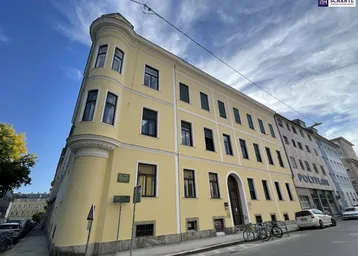 Historisches Gebäude mit markanter runder Ecke und gelber Fassade, gelegen an einer städtischen Straße.