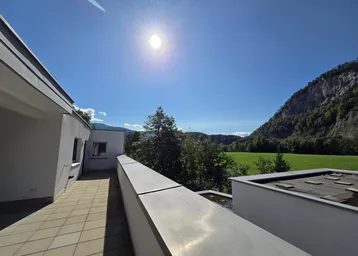 Sonniger Ausblick von der Terrasse auf grüne Wiesen und die majestätische Bergkulisse.