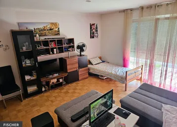 Helles Wohnzimmer mit Parkettboden, Sofa und Zugang zum Balkon, ausgestattet mit einem Bett.