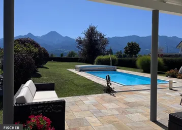 Große Terrasse mit Pool, Gartenmöbeln und beeindruckendem Bergblick unter blauem Himmel.