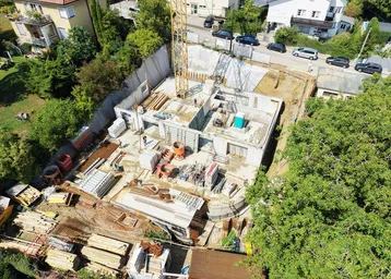 Luftaufnahme einer Baustelle mit Kran und bereits errichteten Fundamenten für ein neues Gebäude.