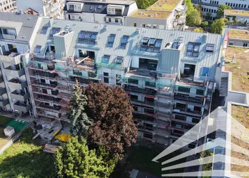 Luftaufnahme eines im Bau befindlichen Gebäudes mit Gerüst und Dachfenstern in städtischer Umgebung.