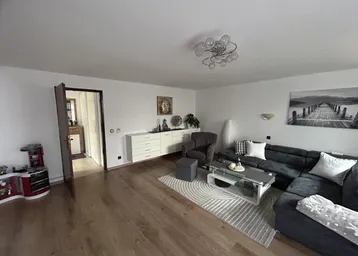 Geräumiges Wohnzimmer mit Holzboden, bequemer Sitzecke und Blick in den Flur.