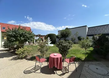 Gemütlicher Gartenbereich mit Sitzgelegenheiten und einem dekorativen Brunnen unter blauem Himmel.