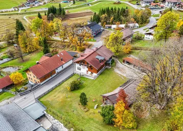 Luftaufnahme eines Anwesens mit mehreren Gebäuden, umgeben von grünen Wiesen und herbstlichen Bäumen.