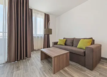 Helles Wohnzimmer mit beigem Sofa, Holztisch und Zugang zu einem Balkon.
