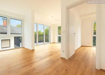 Helles, leeres Wohnzimmer mit Eichenparkettboden und Zugang zu einem Balkon.