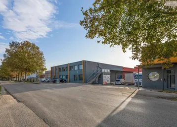 Blick auf die Zufahrtsstraße und die modernen Industriegebäude mit Bäumen im Vordergrund.