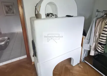 Traditioneller weißer Kachelofen als Heizelement in einem Durchgangsbereich.