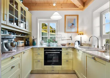 Helle Küche im Landhausstil mit gelben Schränken, Holzbalkendecke und Blick ins Grüne.