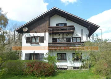 Traditionelles Haus mit weißer Fassade, Holzdetails und mehreren Balkonen in ländlicher Umgebung.