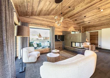 Gemütliches Wohnzimmer im alpinen Stil mit Kamin, Holzwänden und einem Fensterplatz mit Bergblick.