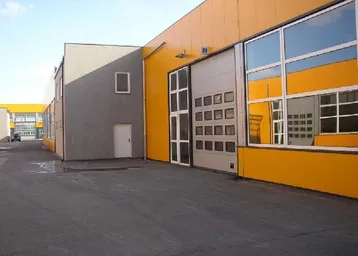 Moderne Gewerbehalle mit gelber Fassade und großen Rolltoren, umgeben von einem asphaltierten Vorplatz.
