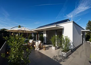 Moderne Architektur mit großer Dachterrasse, Photovoltaikanlage und weitem Blick in die grüne Umgebung.