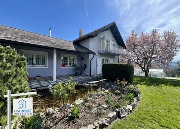 Ansicht des Hauses mit gepflegtem Garten, Teich und blühendem Baum im Frühling.