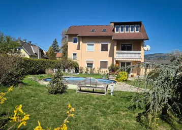 Gepflegter Garten mit Rasenfläche, kleinem Pool und einer Holzbank vor dem Haus.