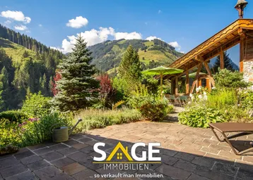 Geräumige Steinterrasse mit Liegestühlen, Sonnenschirm und weitem Blick auf die umliegende Berglandschaft.