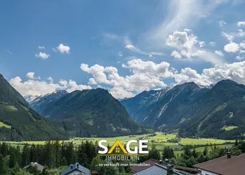 Panoramablick auf die majestätischen Berge und das grüne Tal unter einem weiten blauen Himmel.