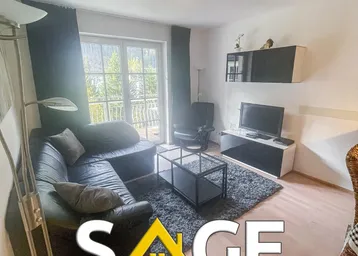 Gemütliches Wohnzimmer mit dunklem Ledersofa, Teppich und Zugang zum Balkon.