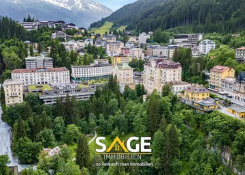 Panoramablick auf eine malerische Stadt in den Bergen mit üppiger Vegetation und einem Wasserfall.