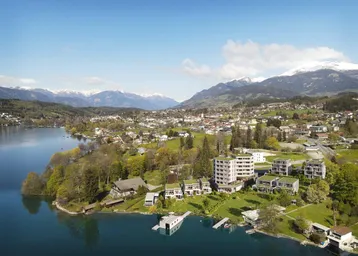 Weitläufige Luftaufnahme einer Stadt am See, umgeben von Bergen und grüner Landschaft unter blauem Himmel.