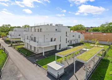 Moderne Wohnanlage mit weißen Fassaden und begrünten Carports unter blauem Himmel.