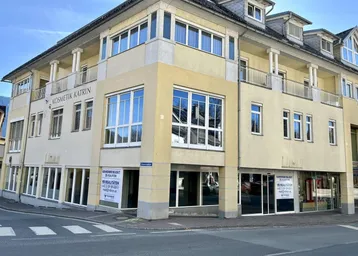 Gebäude mit gelber Fassade und großen Fenstern an einer Straßenecke, mit Gewerbeflächen im Erdgeschoss.