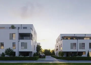Moderne weiße Gebäude mit Flachdach und großen Fenstern, umgeben von Grünflächen bei Sonnenuntergang.