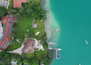 Luftaufnahme eines luxuriösen Anwesens direkt am See mit Bootsstegen und weitläufigen Grünflächen.