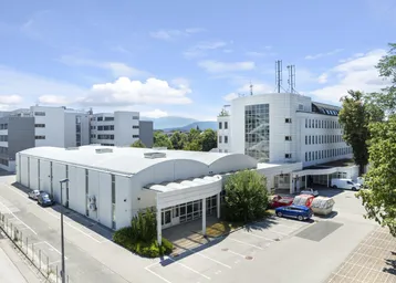 Luftaufnahme eines modernen Büro- und Lagerkomplexes mit Parkplätzen unter blauem Himmel.