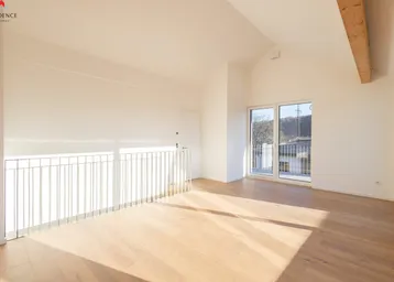 Heller Raum mit Holzboden, Dachschräge und Zugang zu einem kleinen Balkon mit Geländer.