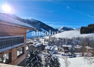 Winterliche Berglandschaft mit schneebedeckten Dächern und einem traditionellen Holzgebäude im Vordergrund.