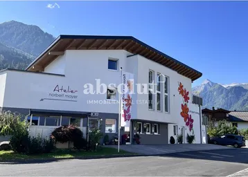 Modernes Gebäude mit weißer Fassade, bunten Blumenmotiven und Bergblick in sonniger Umgebung.