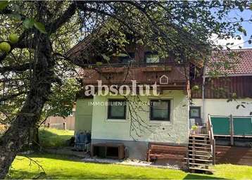 Charmantes Haus mit traditioneller Holzfassade und grünem Gartenbereich umgeben von Bäumen.