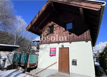 Charmante Chalet-Fassade mit Holzverkleidung und Putz, umgeben von Schnee und mit Bergblick.