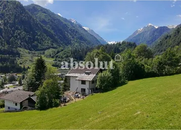 Haus in idyllischer Berglandschaft mit grünen Wiesen und schneebedeckten Gipfeln im Hintergrund