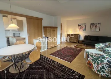 Gemütlicher Wohn-Essbereich mit Holzboden, Teppichen und einem Schrank aus hellem Holz, der den Raum strukturiert.