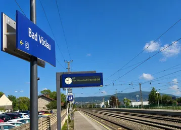 Bahnhof Bad Vöslau mit Gleisen, Bahnsteig und Blick auf die umliegende Landschaft.
